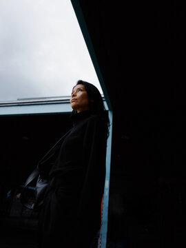 Woman Standing in Urban Area Looking up at the Cloudy Sky