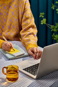 Young woman working on laptop and writing notes in a notebook at home