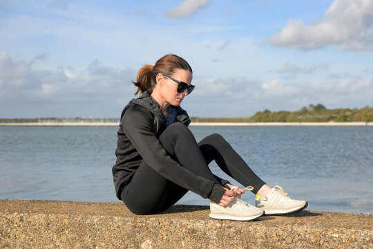 Woman in Athletic Wear Sitting by the Water Tying Laces in Preparation for Running