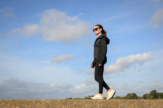 Woman in Athletic Wear Walking Along a Coastal Wall