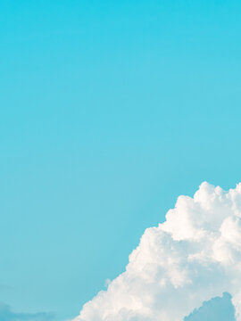 Minimalist bright cyan blue sky with a fluffy white cumulus cloud in the corner, clean summer sky background with large copy space