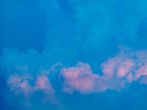 Soft pink tinted clouds glowing at the bottom of a vivid blue sky at dusk, dreamy pastel cotton candy cloudscape background