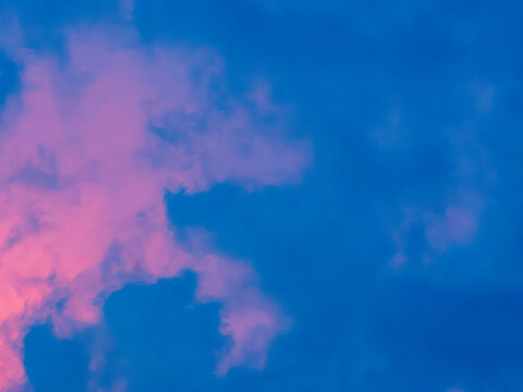 Pink glowing clouds against a deep saturated blue sky at dusk, abstract dreamy pastel cloudscape background with copy space