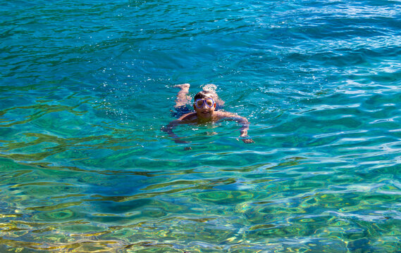 Chico con gafas de buceo nada en el mar sonriendo