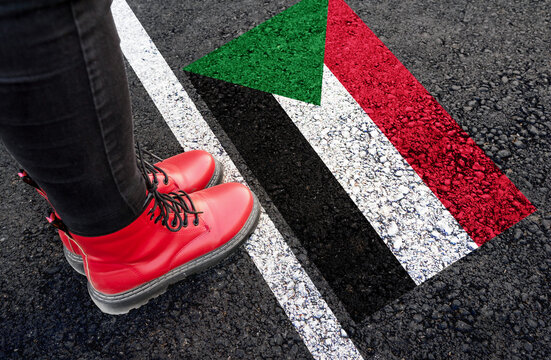 a woman with a boots standing on asphalt next to flag of Sudan and border
