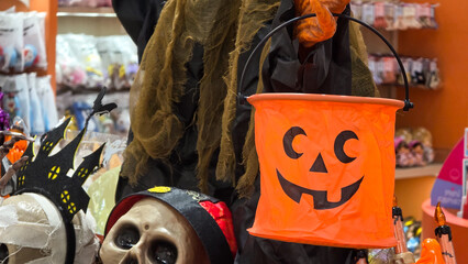 Halloween orange jack o lantern bucket held by witch prop displayed with skull props in a store  © Rungphailin