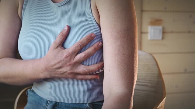 A woman performs a breast self-examination while sitting in an armchair at home. Breast pain, breast cancer, mastopathy, early detection of a breast tumor.