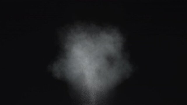 Dusty bullet impact against a wall, sending fragments of debris flying through the air. White powder burst isolated on black background. Explosive hit, scattering dust particles. Cloud of fine debris