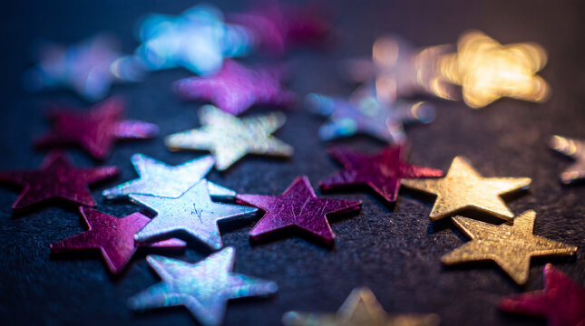 Macro photography of vibrant, multi-colored star-shaped sequins scattered on a dark surface, featuring a dreamy bokeh effect for a festive celebration theme.