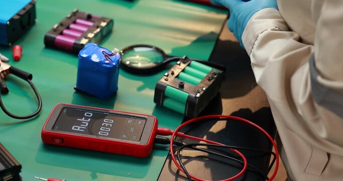 Technician testing rechargeable battery packs with a digital meter and probe leads on an electronics workbench.