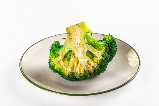 Roasted broccoli floret on ceramic plate showing charred edges and vibrant green texture as healthy vegetable dish