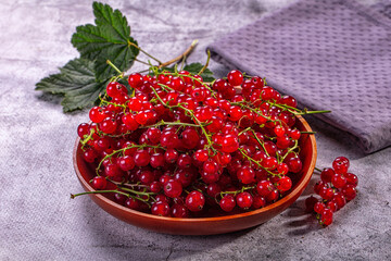 Red currant berries in brown wooden bowl with green leaves on grey textured cloth, fresh summer fruit © Andrei Starostin