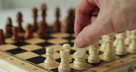 Hand moves chess piece on wooden board during focused play. Chess moment shows decision making and control. Chess strategy reflects thinking process. Close view of chess supports leadership, planning © julia_diak