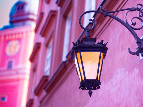 Illuminated vintage street lantern on pink wall of historic building