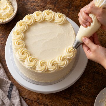 Decoraci&oacute;n de una tarta redonda con crema usando una manga pastelera sobre una mesa de madera