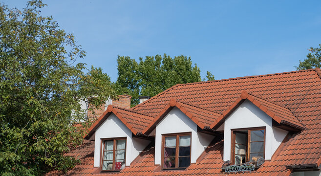 A traditional red tiled roof with dormer windows and a ginger cat sitting on the open windowsill in Kazimierz Dolny, Poland.