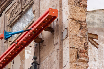 Orange steel scaffolding beam against ornate historic facade with Greek meander cornice during restoration, Valencia Spain © Egor Terentev