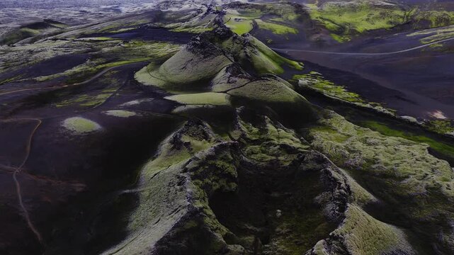 Aerial view showcases the Lakagigar volcanic fissure row in Iceland, where moss covered craters rise above vast black lava fields under overcast daylight.