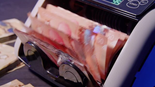 Counting machine sorts and tallies a stack of banknotes in a close-up view of cash handling