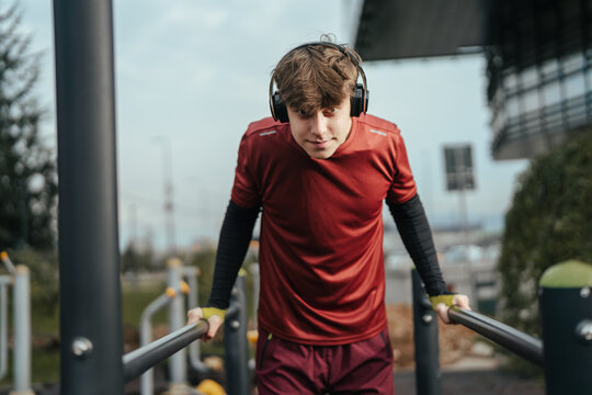 Young man training outdoors doing dips on parallel bars