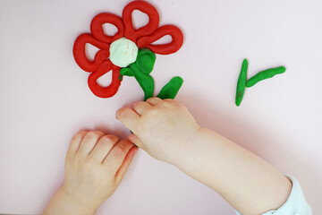 Child’s hands modeling a bright plasticine flower on a pastel background. Useful for promoting creativity development, fine motor skills education, and early childhood learning materials. © Irina