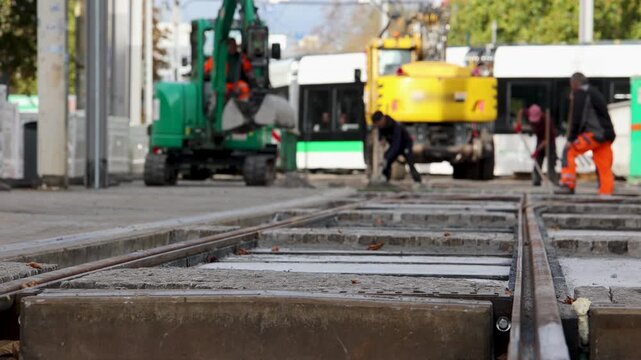 Municipal workers repair tram tracks in Magdeburg, Germany, using excavator and construction machinery. Close view of railway rails and concrete sleepers shows urban infrastructure maintenance
