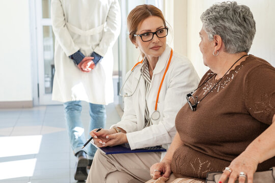 A female doctor talks with a patient who is waiting in the hospital hallway for their appointment. The conversation feels calm and friendly as they discuss the upcoming examination.