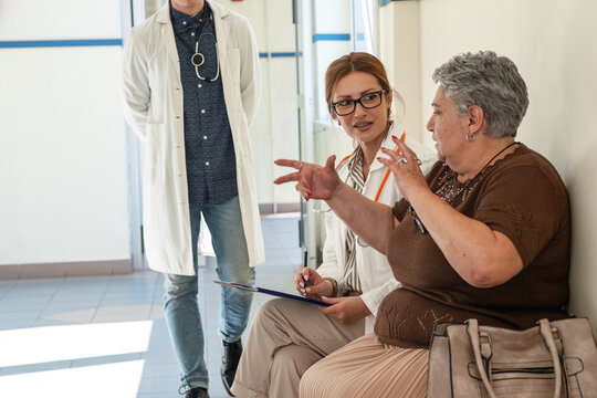 A female doctor talks with a patient who is waiting in the hospital hallway for their appointment. The conversation feels calm and friendly as they discuss the upcoming examination.