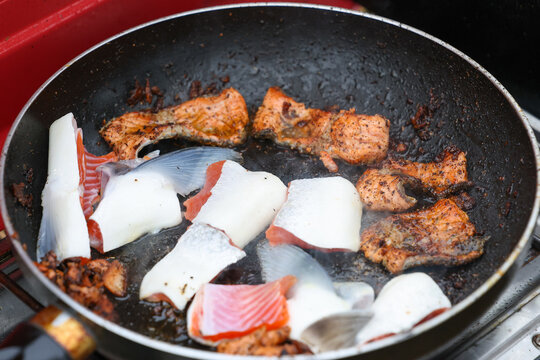 Fresh coho salmon fillet medallions cooking on a hot skillet beside a river in Alaska. The tasty red seafood is cooking outside on the tundra. 