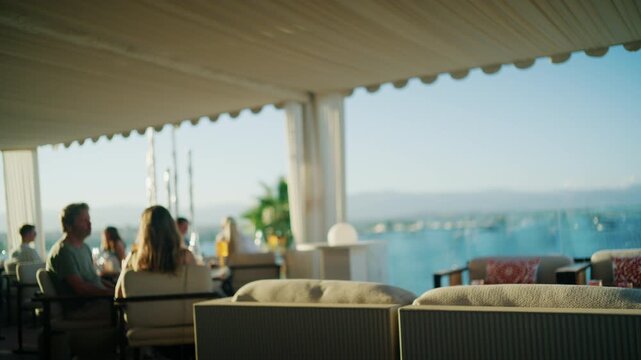 Blurred diners sitting on an elegant rooftop terrace under a scalloped awning overlooking the blue bay, French Riviera, France.