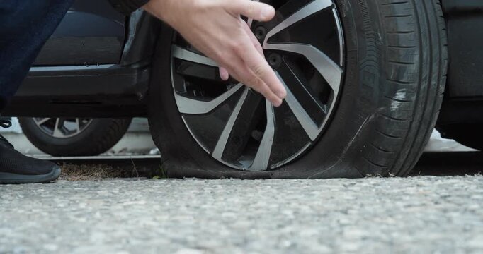 Close up of a hand checking a flat car tire beside the wheel