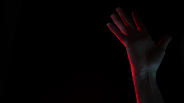 Spooky close-up shot of a mysterious hand emerging from total blackness with vivid red highlights