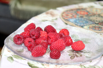 Clear glass plate with ripe red raspberries on a table, dessert – horizontal photo, close-up © Iuliia Koroleva