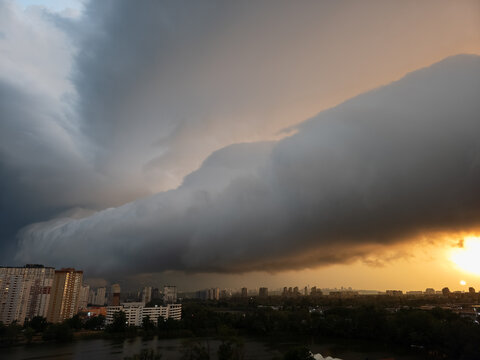 Kyiv, Ukraine's Darnitskyi district displays towering residential high-rises and a tranquil lake, dynamically lit by a golden sunset sky against a massive storm shelf cloud