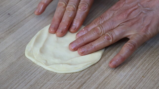 Hands flattening an oiled dough ball for Moroccan msemen