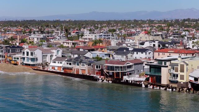 Long Beach, California, USA - October 15, 2026: Wide view of boarded up homes behind sandbags and the battered seawall as an excavator piles sand into a flood berm after Tropical Storm Rachel.