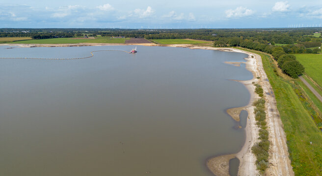 Industrial sand mining landscape near Borger, Drenthe, capturing the dredging boat at work in the pit lake with shallow sandbanks and a roadside tree line visible on the right