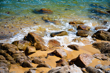 Foamy turquoise waves wash across rocks and golden sand on a rugged coastal shoreline © Tom Harwood