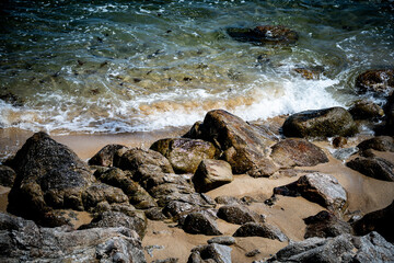 Clear ocean waves wash over sunlit rocks and sand along a rugged natural shoreline © Tom Harwood