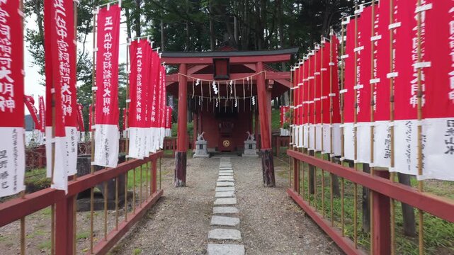 Rows of traditional red banners lead to a small Inari shrine with stone fox statues at Nikko Futarasan-jinja Chugushi Shrine in Nikko, Japan.