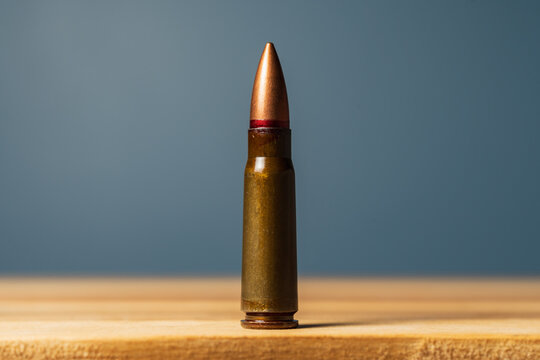 Single 7.62x39mm rifle cartridge with steel case and red lacquer sealant standing vertically on wooden table against dark background.