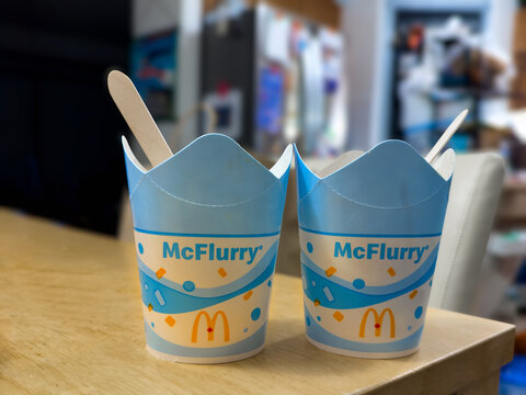 Calgary, AB, Canada. Oct 17, 2026. Eye-level view of two McDonald's McFlurry ice cream cups with wooden spoons sitting on wooden counter.