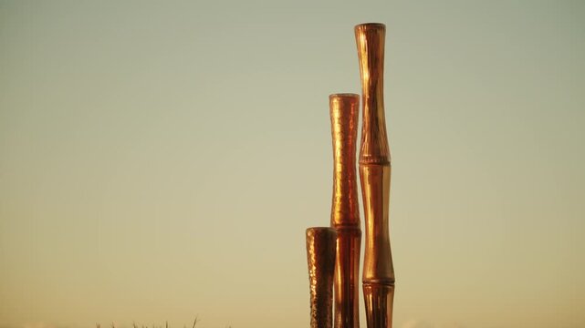 Three tall copper glass bamboo-shaped vases glowing against a gradient sunset sky with copy space, French Riviera, France.