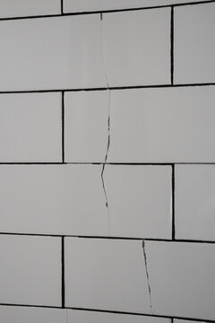 Vertical fracture crosses white bathroom wall tiles after earthquake movement, revealing structural stress, damaged ceramic, unstable masonry and urgent need for professional building inspection.