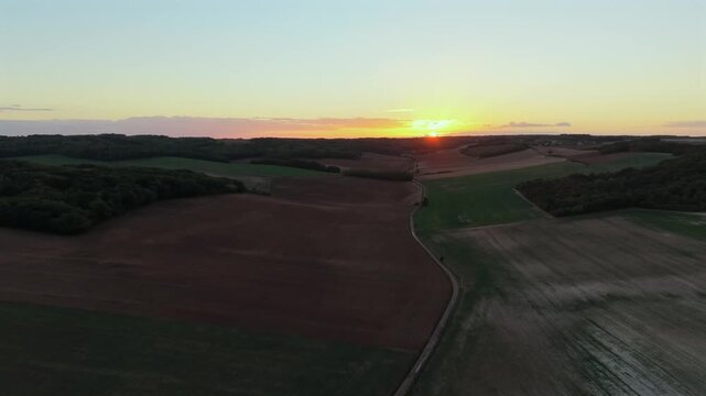 Aerial traveling shot over countryside road and fields at sunset