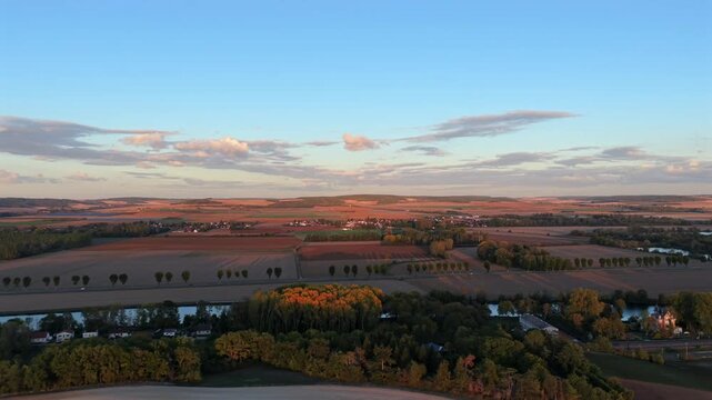 Aerial traveling shot over autumn fields, river and tree-lined road