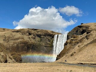 Skógafoss waterfall with rainbow and blue sky with white clouds on rocky cliff, Iceland © Kate