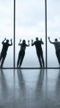 Playful team silhouettes pressing hands against a floor to ceiling window facing a misty horizon