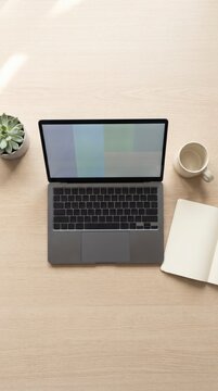 Overhead view of a laptop, notebook and coffee mug on a light wood desk with a small succulent