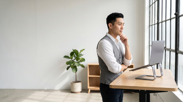 Problem solving developer standing at an ergonomic desk with hand on chin, deep in thought